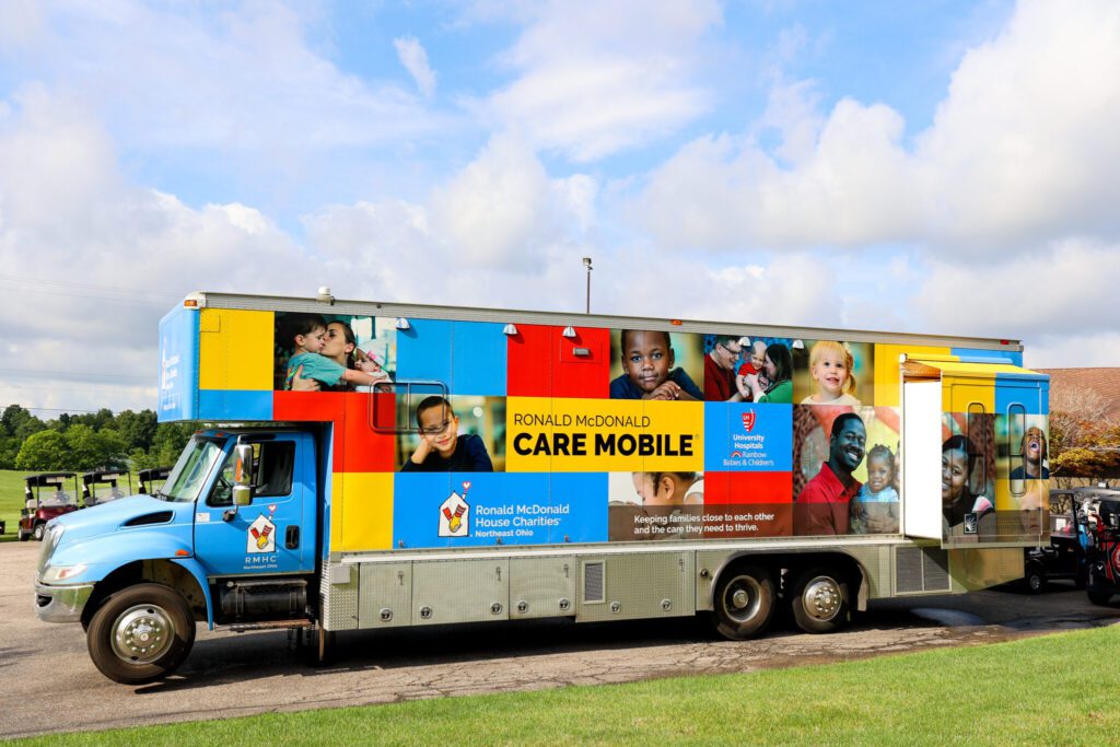 The Ronald McDonald Care Mobile is a mobile dental clinic for children in partnership with UH Rainbow Babies & Children’s Hospital. Pictured here, the outside is decorated in a square pattern of red, yellow, and blue, with pictures of smiling children and their parents. The Ronald McDonald House Charities of Northeast Ohio logo appears on the side along with Ronald McDonald Care Mobile in large black type on a yellow square.