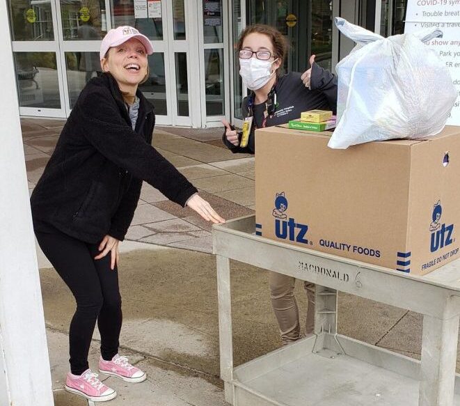 Two young women with donations smile for the camera. They're pushing a beige plastic cart with a big box on it