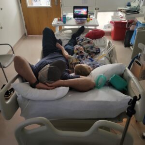 man laying next to little boy in hospital bed