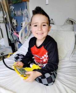 boy in hospital bed with machines and holding game