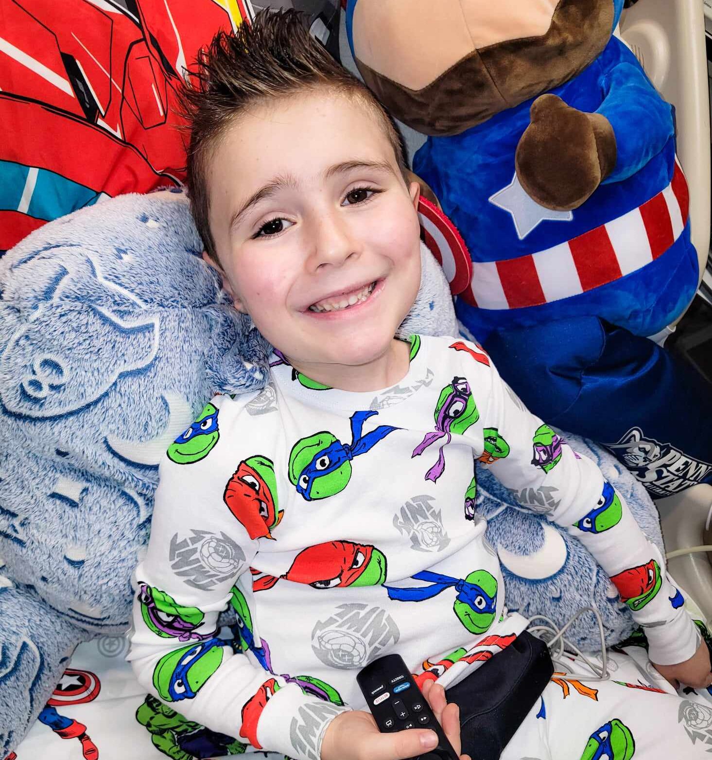 Young boy with punky slicked up hair and ninja turtles pajamas rests in bed with stuffed animals
