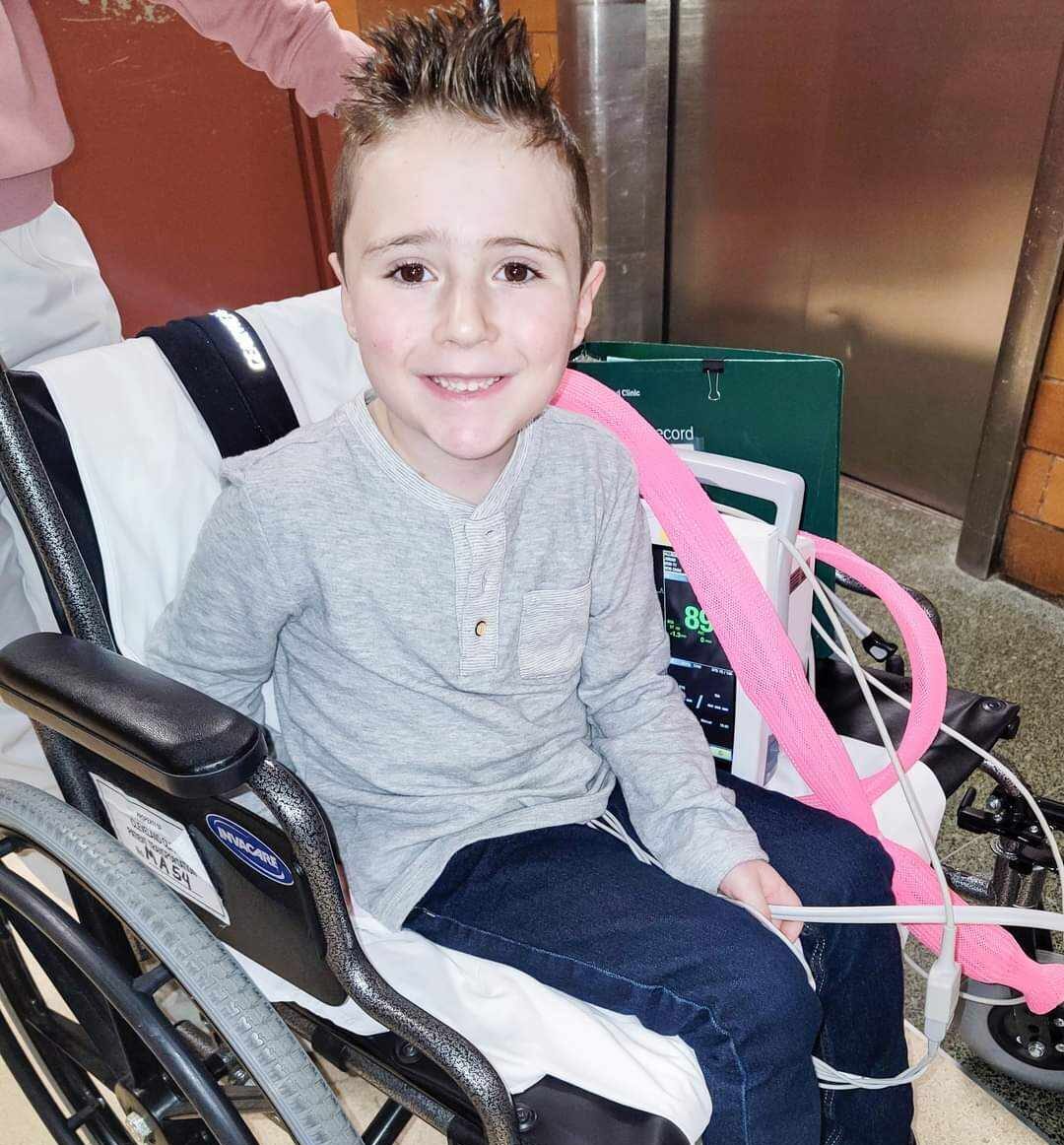 Young boy smiling, seated in wheelchair, with monitors attached