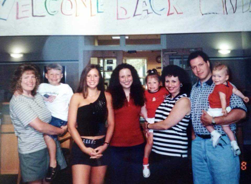 Family of eight, five teens/adults and three children, in front of Ronald McDonald House registration desk with welcome back sign