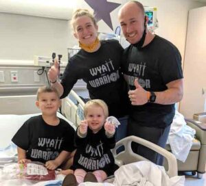 Family around hospital bed giving thumbs up