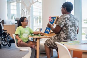 A young girl watches intently during a lesson with a female staff member. They are seated at a table in the STAR Center.