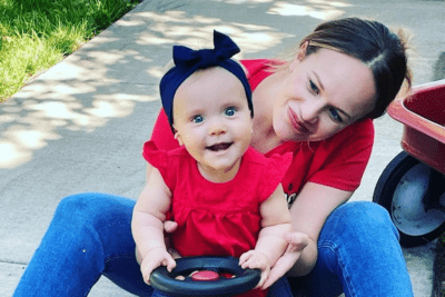Baby and mom smiling and riding toy on sidewalk