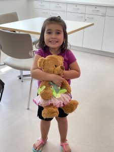 A young girl in the kitchenette smiles and hugs a teddy bear. 