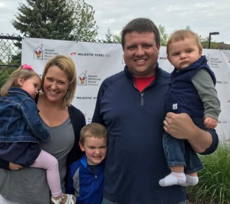 A man and a woman with their three children posing in front of an RMHC sign.