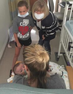 women sitting down holding baby while a little girl and woman say hi to baby