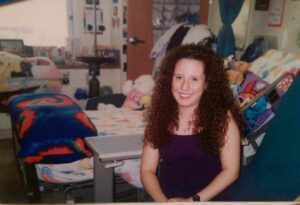 woman sitting on hospital bed smiling. children's blankets and colorful accents in room