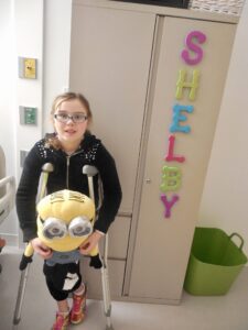 little girl on crutches holding minion stuffed animal