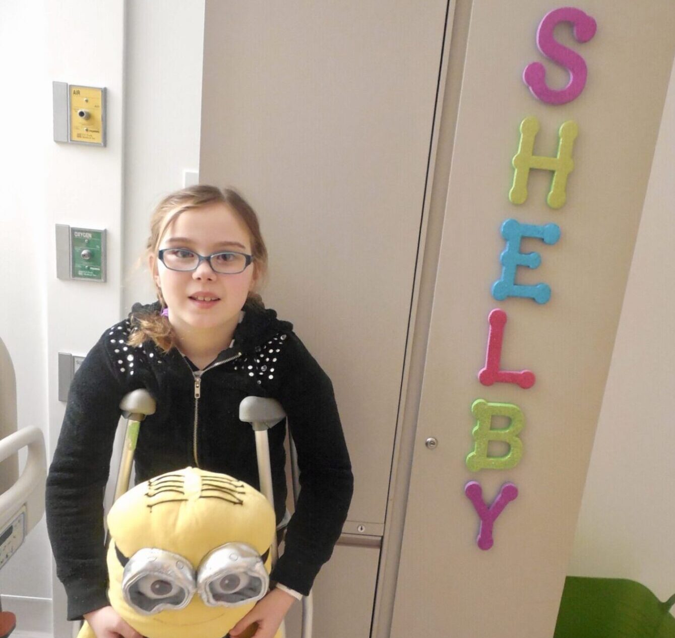 little girl on crutches holding minion stuffed animal