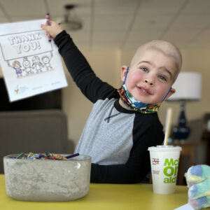 Wyatt, a yound child, holds up crayon drawing that says "thanks"
