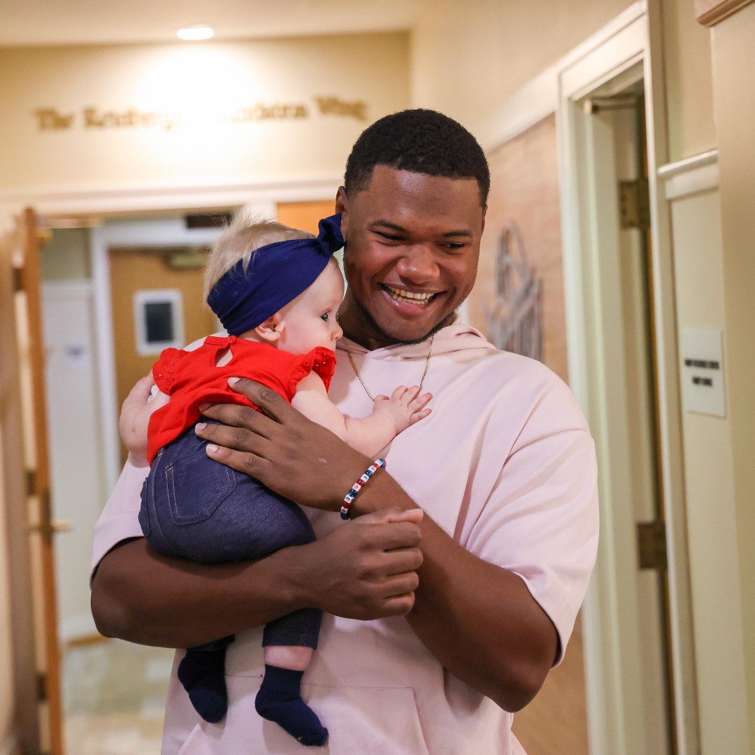 Cleveland Guardians player Oscar Gonzalez carrying a baby in the Ronald McDonald House.