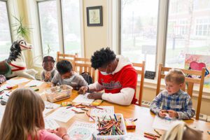 Oscar Gonzalez coloring with children in the Cleveland House sunroom.