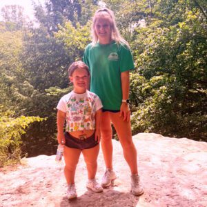 Shae and her sister standing on a large rock in the mountains during a hike.