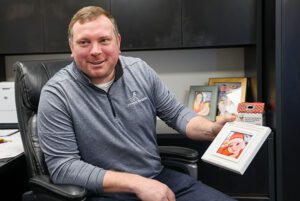 Tylor Mettler sits at his desk, holding a photo of his baby daughter