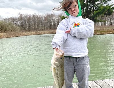 Shae standing on a dock with a lake in the background, holding a big fish she caught